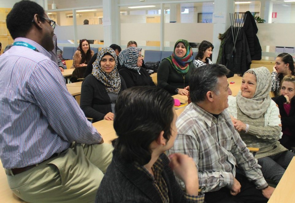 Pakolaisavun omakielisen yhteiskuntaorientaatiokurssin osallistujat istuvat ja keskustelevat luokkahuoneessa ohjaajan kanssa