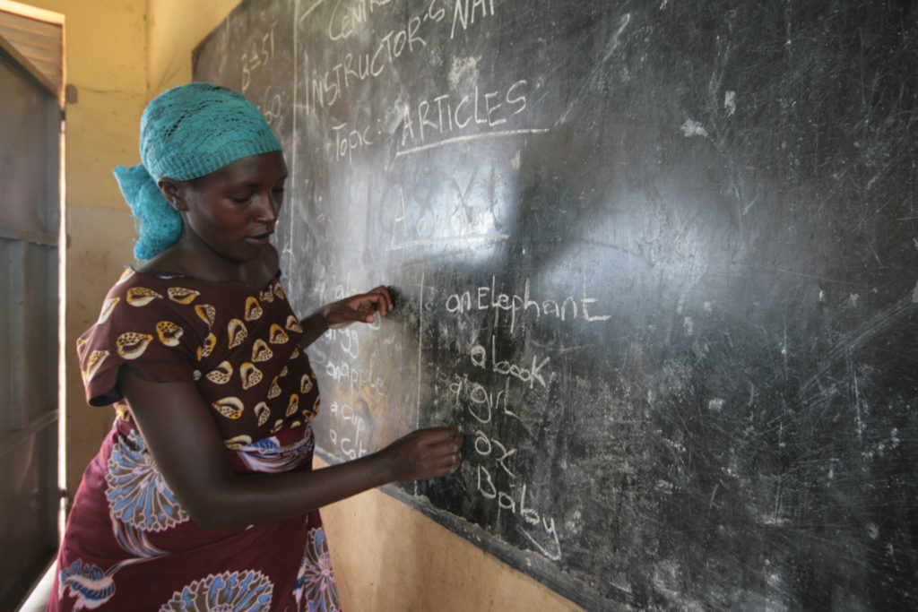 Nainen kirjoittaa liitutaululle Pakolaisavun englannin kielen tunnilla Ugandassa