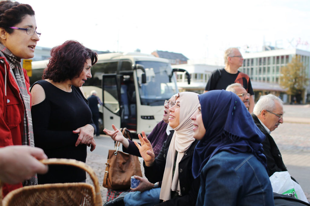 Maahanmuuttajataustaiset naiset keskustelevat iloisesti ulkona sijaitsevalla aukiolla