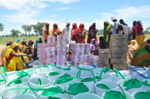 Sudanin pakolaisleirillä joukko ihmisiä on kerääntynyt jaettavien tarvikkeiden, kuten vesiämpäreiden ja elintarvikkeiden, ympärille.