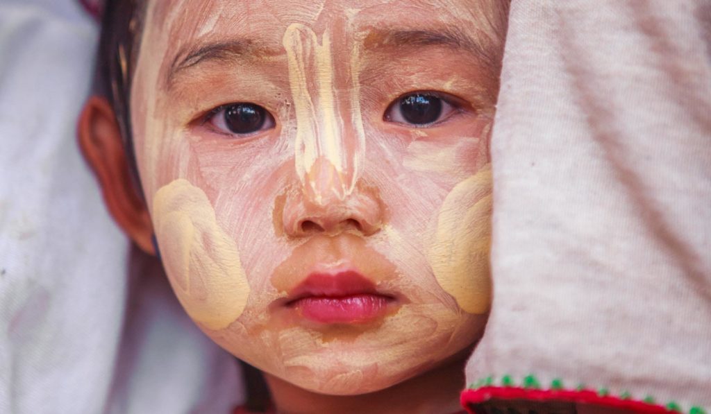 Myanmarilaisen lapsen, jonka kasvot ovat maalattu, katsoo kameraan
