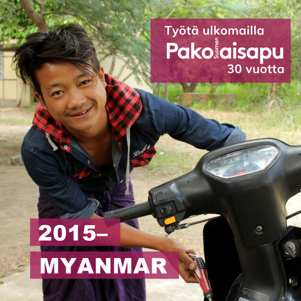 Mies korjaa mopoa ja hymyilee kameralle. Kuvassa on Pakolaisapu, työtä ulkomailla 30 vuotta -logo ja teksti Myanmar 2015-.