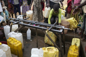 Lapsi kumartuu täyttämään kanisteria vesipisteellä Ugandan Nakivalessa.
