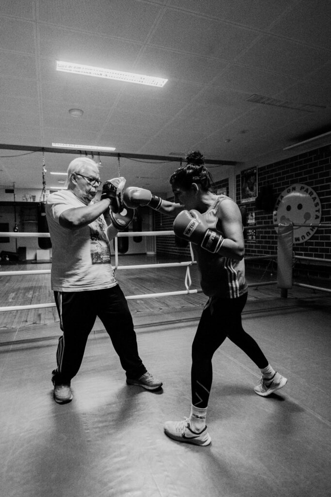 Mustavalkoinen kuva nuoresta naisesta ja vanhemmasta silmälasipäisestä miehestä, jotka harjoittelevat nyrkkeilyä.