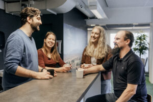 Neljä ihmistä kahvikuppien kanssa keittiössä, keskustelevat hymyillen.