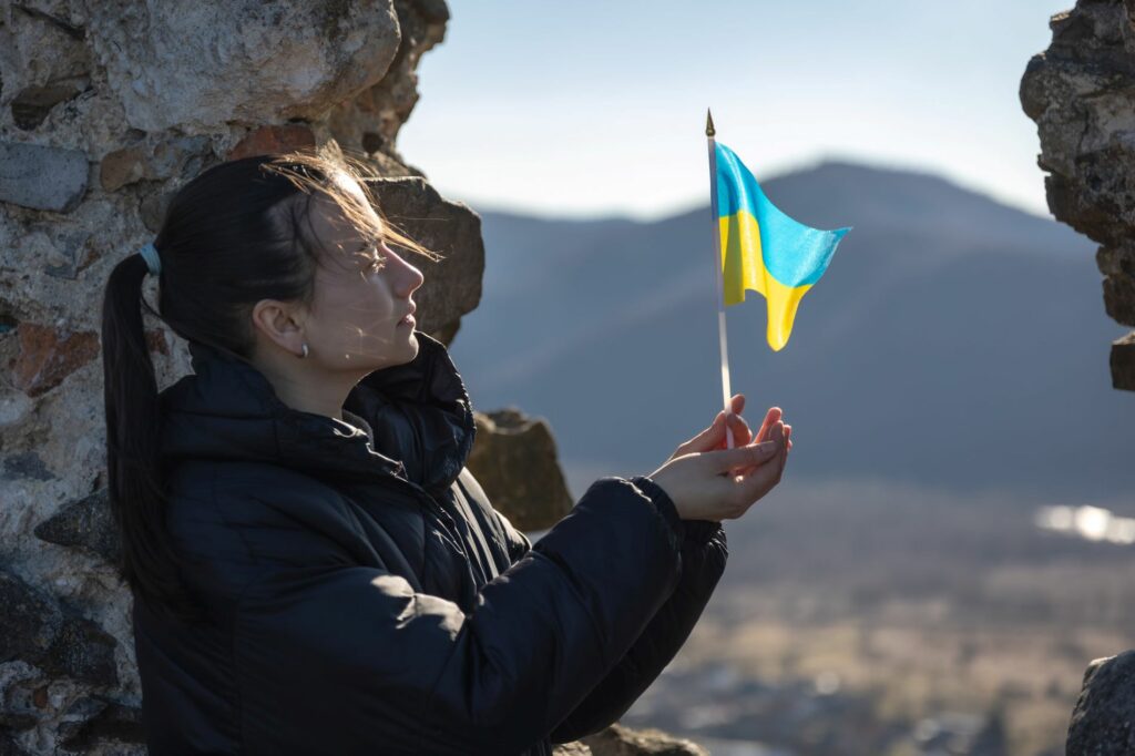 Nainen seisoo ulkona ja pitää käsissään pientä Ukrainan lippua.