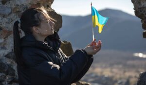 Nainen seisoo ulkona ja pitää käsissään pientä Ukrainan lippua.