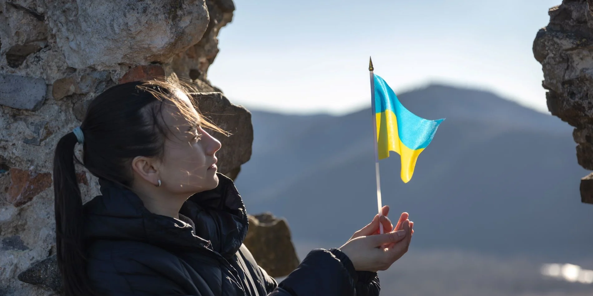Nainen seisoo ulkona ja pitää käsissään pientä Ukrainan lippua.