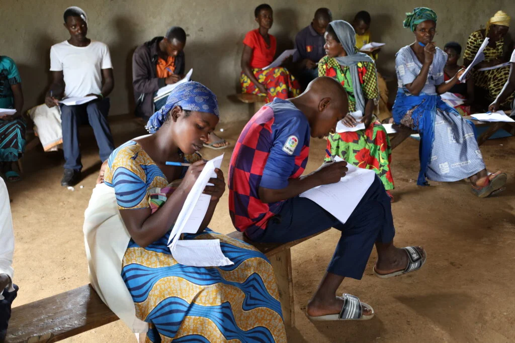 Cose up of a learner writing an exam in Kyaka II Refugee Settlment in South Western Uganda. There are other learners in the background.