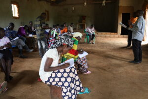 Close up of a learner writing an exam in Uganda. There are other learners in the background.